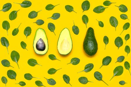 Ripe sliced avocado and spinach leaves on yellow background top view. Creative food composition Flat lay. Pop art design, tropical summer abstract background with avocado. Green avocadoes pattern.の写真素材