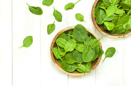 Fresh green spinach leaves on wooden bowl on white wooden rustic background top view copy space. Baby young spinach leaves, Ingredient for salad, healthy food, diet. Nutrition conceptの写真素材