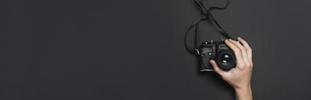 Male hands hold old vintage camera on black background top view flat lay with copy space. Concept for the photographer, old photographic equipment, minimalistic style.の写真素材