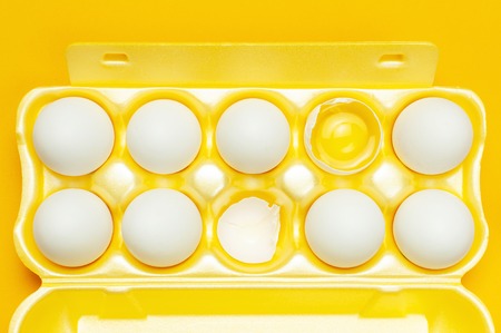 White chicken eggs in yellow packaging on yellow background top view flat lay copy space. Eggs in box, natural healthy food and organic farming concept. Creative food minimalistic background, Easter.の写真素材
