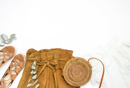 Female fashion background. Stylish trendy feminine summer clothing set. Shorts, white jacket, sandals, round rattan bag, sprig eucalyptus on white background. Trendy hipster look Flat lay top view.の写真素材