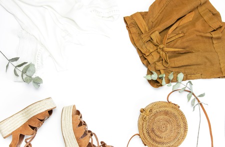 Female fashion background. Stylish trendy feminine summer clothing set. Shorts, white jacket, sandals, round rattan bag, sprig eucalyptus on white background. Trendy hipster look Flat lay top view.の写真素材