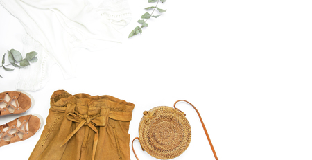 Female fashion background. Stylish trendy feminine summer clothing set. Shorts, white jacket, sandals, round rattan bag, sprig eucalyptus on white background. Trendy hipster look Flat lay top view.の写真素材