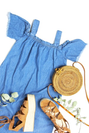 Stylish trendy feminine summer clothing denim dress sundress, sandals round rattan bag sprig eucalyptus on white background Trendy hipster look Female fashion background blog concept Flat lay top view.の写真素材