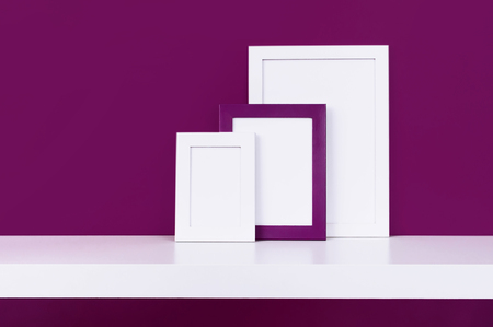 Three wooden empty frames for a photo on a white shelf on a background of a bright purple red wall. Blank paper frames, modern home decor mock-upの写真素材