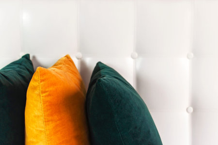 Bright decorative soft pillows in bed on the background of leather quilted headboard. Emerald and...