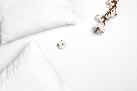 Soft white quilted pillow and branch of cotton on light background top view. Clean pillow, interior item, bedding mockup design template.の写真素材