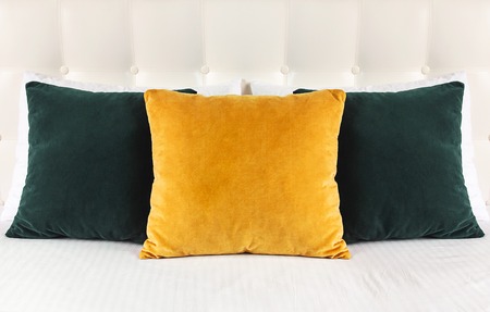 Bright decorative soft pillows in bed on the background of leather quilted headboard. Emerald and orange pillow, part of bed close-up, comfort. Quilted headboard background, interior.の写真素材