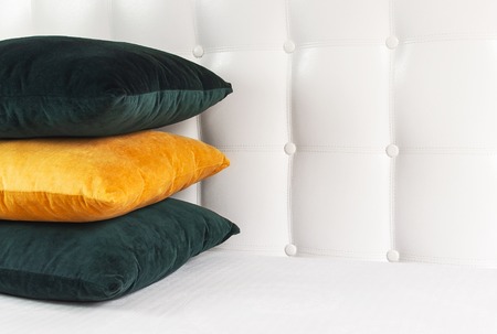 Bright decorative soft pillows in bed on the background of leather quilted headboard. Emerald and orange pillow, part of bed close-up, comfort. Quilted headboard background, interior.の写真素材