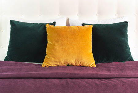 Bright decorative soft pillows in bed on the background of leather quilted headboard. Emerald and orange pillow, part of bed close-up, comfort. Quilted headboard background, interior.の写真素材