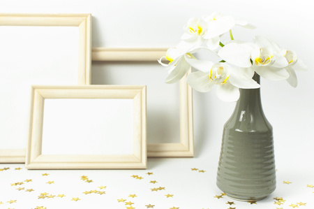 White Phalaenopsis orchid flowers in gray vase, wooden photo frames, golden stars confetti on white background. Branch of Tropical flower flat lay. Interior details Layout for design Mockup.の写真素材