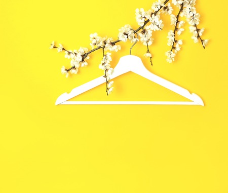 White wooden hanger hanging on the spring flowering branch on yellow background. Spring sale concept discount store shopping empty hanger. Creative fashion beauty banner. Flat lay top view copy spaceの写真素材