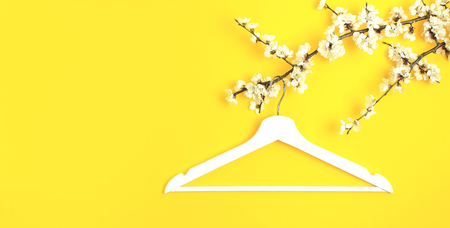 White wooden hanger hanging on the spring flowering branch on yellow background. Spring sale concept discount store shopping empty hanger. Creative fashion beauty banner. Flat lay top view copy spaceの写真素材