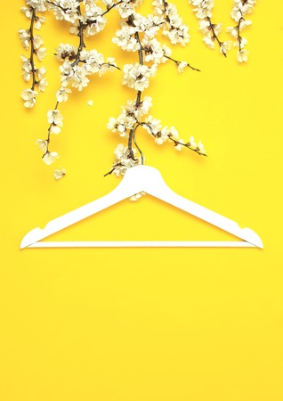 White wooden hanger hanging on the spring flowering branch on yellow background. Spring sale concept discount store shopping empty hanger. Creative fashion beauty banner. Flat lay top view copy spaceの写真素材