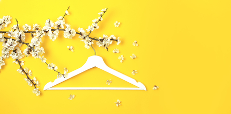 White wooden hanger hanging on the spring flowering branch on yellow background. Spring sale concept discount store shopping empty hanger. Creative fashion beauty banner. Flat lay top view copy spaceの写真素材
