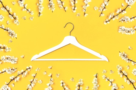 White wooden hanger and spring flowering branch on yellow background. Spring sale concept discount store shopping empty hanger promo design. Creative fashion beauty banner Flat lay top view copy spaceの写真素材