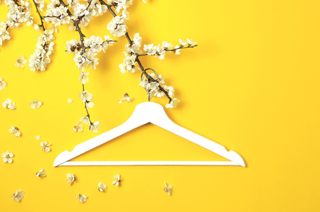 White wooden hanger hanging on the spring flowering branch on yellow background. Spring sale concept discount store shopping empty hanger. Creative fashion beauty banner. Flat lay top view copy spaceの写真素材