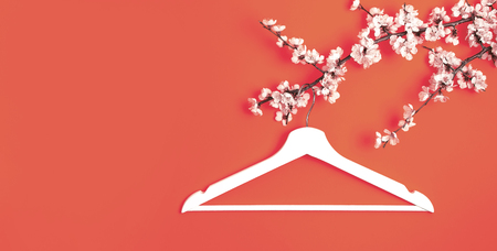 White wooden hanger hanging on the spring flowering branch on coral background. Spring sale concept discount store shopping empty hanger. Creative fashion beauty banner. Flat lay top view copy spaceの写真素材