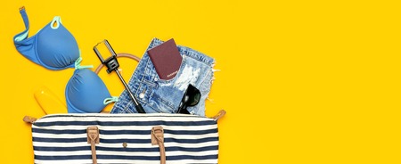 Female summer clothing accessories on yellow background. Concept of travel vacation sea Striped Nautical Bag swimming suit denim shorts sunglasses sunscreen passport phone self-stick Flat lay top view.の写真素材