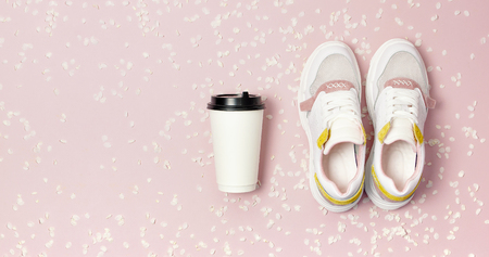 Female Fashionable Sneakers, Coffee or tea paper cup and spring branches of white flowers on pink background top view flat lay. Take away coffee cup, mockup. Creative spring background, lifestyle.の写真素材