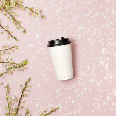 Coffee or tea paper cup and spring branches of white flowers of cherry on pink background top view flat lay. Take away coffee cup, mockup. Creative spring background, layout for design, lifestyle.の写真素材