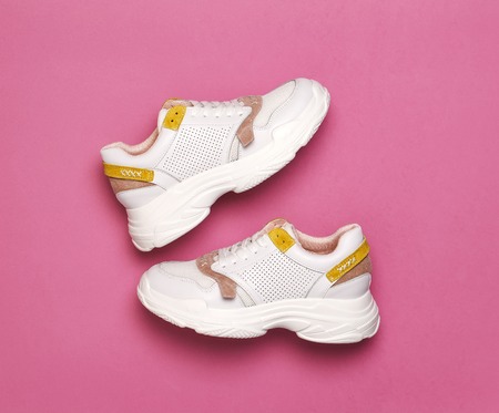 White female sneakers on bright pink background. Fashion blog or magazine concept. Women shoes, trendy sneakers, fashion, style, lifestyle.の写真素材
