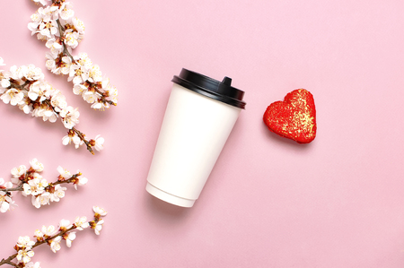 Coffee or tea paper cup, heart-shaped macaroon cakes, spring branches of white flowers on pink background top view flat lay. Take away coffee cup, mockup. Coffee love concept, layout for design.の写真素材
