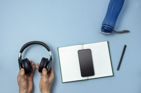 Mens hands holding headphones, blue sneakers, bottle of waters smartphone notebook diary with marker on blue background.の写真素材