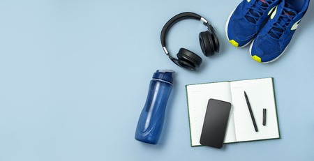 Mens blue sneakers, bottle of waters, smartphone, headphone, notebook diary with marker on blue background.の写真素材