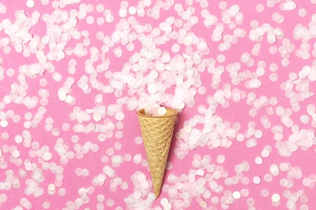 Waffle cone with bouquet of round confetti on pastel pink background. Festive holiday background, concept of party, birthday. Creative holiday concept minimal style Flat lay top view.の写真素材