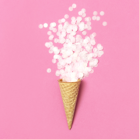 Waffle cone with bouquet of round confetti on pastel pink background. Festive holiday background, concept of party, birthday. Creative holiday concept minimal style Flat lay top view.の写真素材