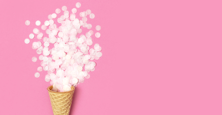 Waffle cone with bouquet of round confetti on pastel pink background. Festive holiday background, concept of party, birthday. Creative holiday concept minimal style Flat lay top view.の写真素材