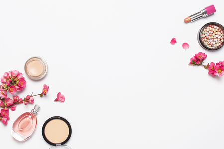 Different makeup cosmetic. Ball blush rouge face powder lipstick concealer bottle of perfume eyeshadow makeup brush spring pink flowers on light background top view flat lay. Beauty fashion background.の写真素材