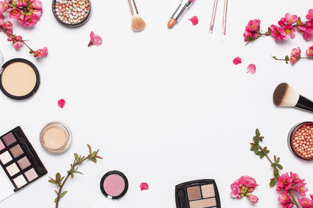 Different makeup cosmetic. Ball blush rouge face powder lipstick concealer bottle of perfume eyeshadow makeup brush spring pink flowers on light background top view flat lay. Beauty fashion background.の写真素材