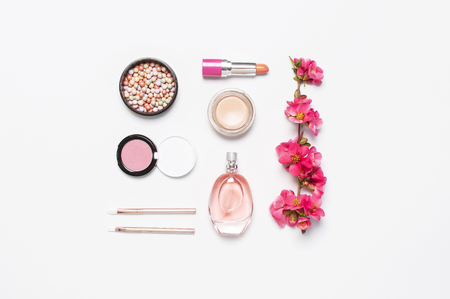 Different makeup cosmetic. Ball blush rouge face powder lipstick concealer bottle of perfume eyeshadow makeup brush spring pink flowers on light background top view flat lay. Beauty fashion background.の写真素材