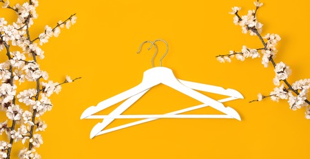 Creative fashion beauty background. White wooden hangers and spring flowering branch on yellow background. Spring sale concept discount store shopping empty hanger promo design Flat lay top view.の写真素材