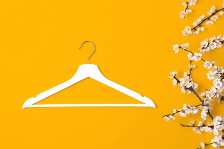 Creative fashion beauty background. White wooden hanger and spring flowering branch on yellow background. Spring sale concept discount store shopping empty hanger promo design. Flat lay top view.の写真素材