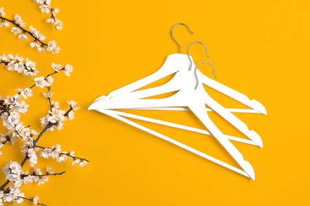 Creative fashion beauty background. White wooden hangers and spring flowering branch on yellow background. Spring sale concept discount store shopping empty hanger promo design Flat lay top view.の写真素材