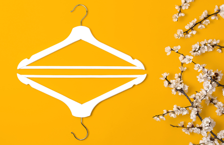 Creative fashion beauty background. White wooden hangers and spring flowering branch on yellow background. Spring sale concept discount store shopping empty hanger promo design Flat lay top view.の写真素材