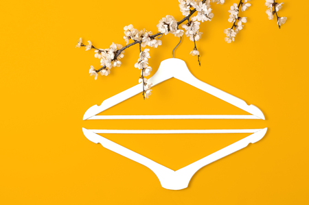 Creative fashion beauty background. White wooden hanger hanging on the spring flowering branch on yellow background. Spring sale concept discount store shopping empty hanger. Flat lay top view.の写真素材