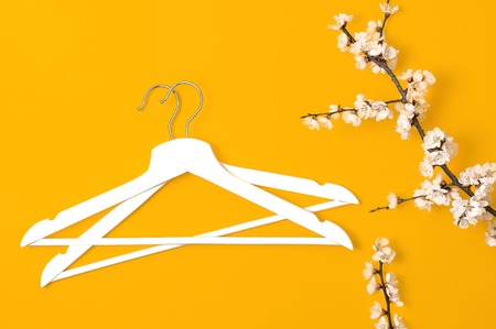 Creative fashion beauty background. White wooden hangers and spring flowering branch on yellow background. Spring sale concept discount store shopping empty hanger promo design Flat lay top view.の写真素材