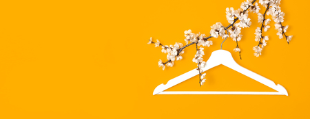 Creative fashion beauty background. White wooden hanger hanging on the spring flowering branch on yellow background. Spring sale concept discount store shopping empty hanger. Flat lay top view.の写真素材