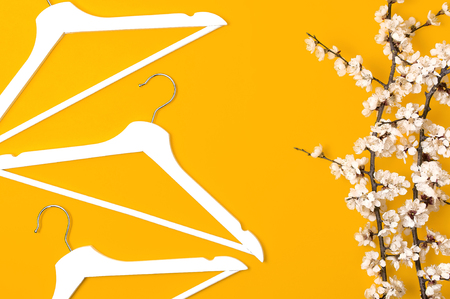 Creative fashion beauty background. White wooden hangers and spring flowering branch on yellow background. Spring sale concept discount store shopping empty hanger promo design Flat lay top view.の写真素材