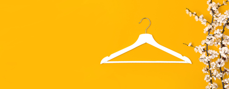 Creative fashion beauty background. White wooden hanger and spring flowering branch on yellow background. Spring sale concept discount store shopping empty hanger promo design. Flat lay top view.の写真素材