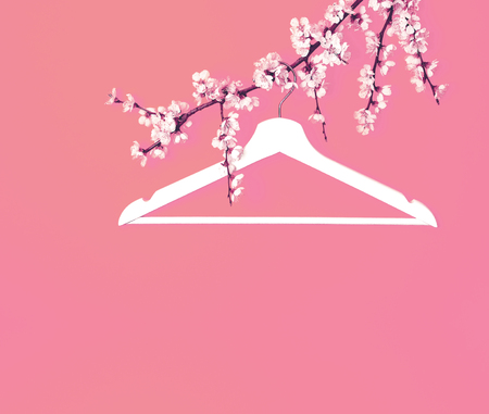 Creative fashion beauty concept. White wooden hanger hanging on the spring flowering branch on pink background. Spring sale concept discount store shopping empty hanger. Flat lay top view copy spaceの写真素材