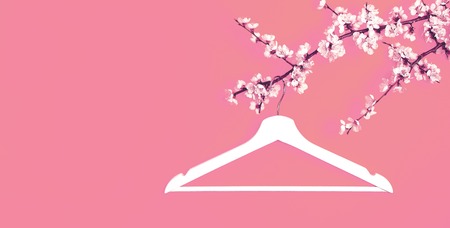 Creative fashion beauty concept. White wooden hanger hanging on the spring flowering branch on pink background. Spring sale concept discount store shopping empty hanger. Flat lay top view copy spaceの写真素材