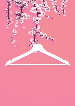 Creative fashion beauty concept. White wooden hanger hanging on the spring flowering branch on pink background. Spring sale concept discount store shopping empty hanger. Flat lay top view copy spaceの写真素材