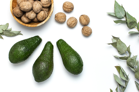 Ripe fresh avocado, walnuts in wooden bowl, eucalyptus twigs on white background top view Flat lay copy space. Fruits Healthy food concept, diet, healthy lifestyleの写真素材