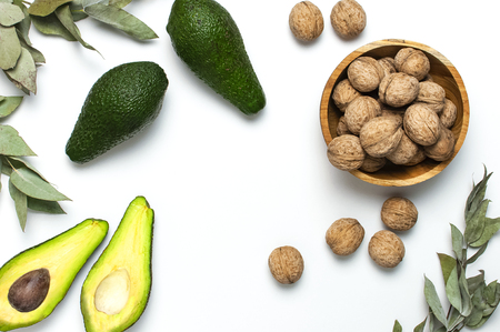 Ripe fresh avocado, walnuts in wooden bowl, eucalyptus twigs on white background top view Flat lay copy space. Fruits Healthy food concept, diet, healthy lifestyleの写真素材