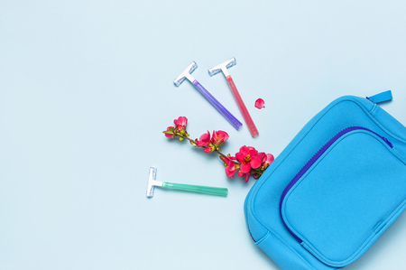 Women's multi-colored disposable razors, cosmetic bag, pink flowers on a pastel blue background, top view Flat lay copy space. Skin care concept, female cosmetic accessory. Shaving razor instrumentの写真素材